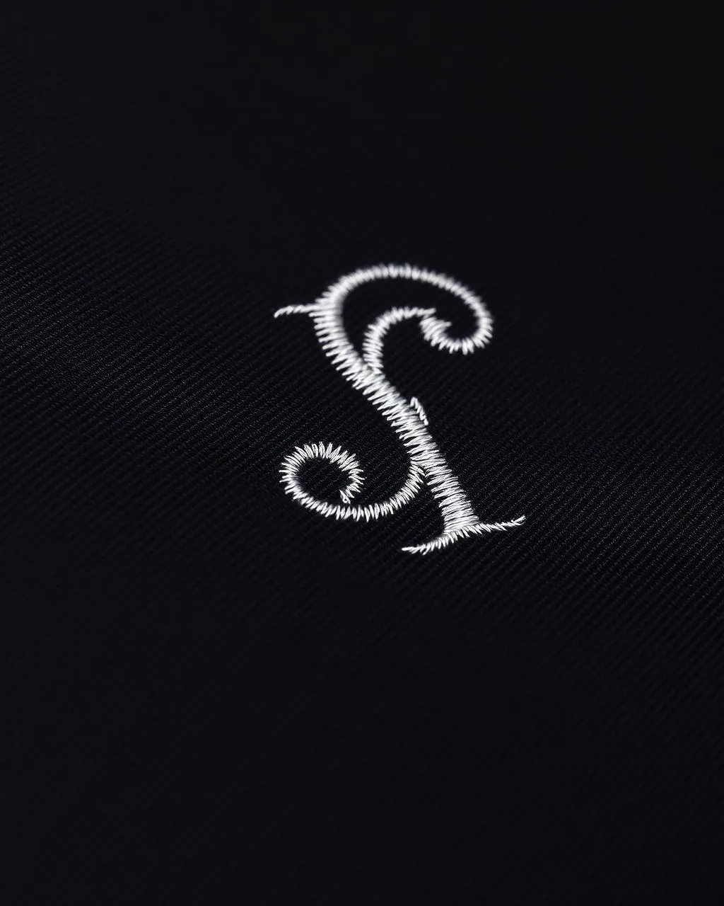 Weißes gesticktes Monogramm auf schwarzem Stoff